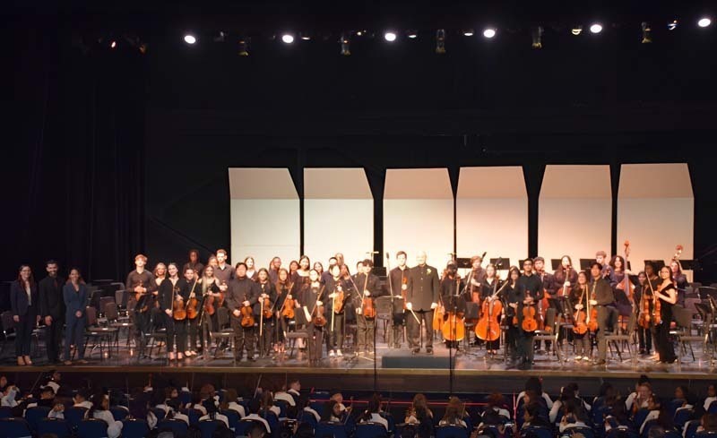 An orchestra performing while a conductor leads them