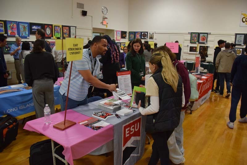 People talking at a college fair booth in the gym